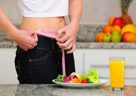 A girl losing weight on a diet measures her waist size